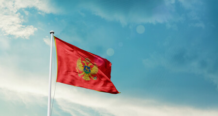 Waving Flag of Montenegro in Blue Sky. The symbol of the state on wavy cotton fabric.