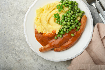 Bangers and mash. Grilled sausages with mash potato and green pea on white plate on grey background. Traditional dish of Great Britain and Ireland. BBQ beef sausages. Top view.