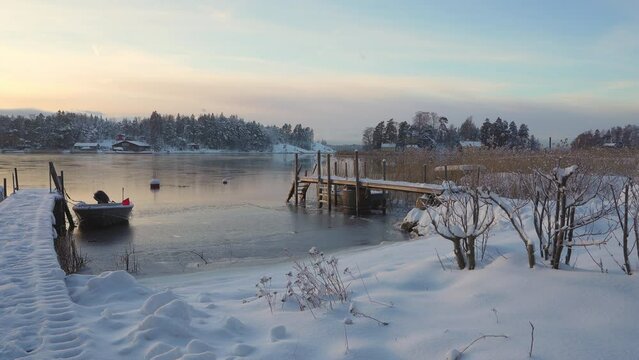 Soukka, Finland - 09.12.22: View from the shore of a small snow-covered island with houses. Frozen bay. Two wooden piers and a boat in the foreground. Winter landscape. Scandinavia.