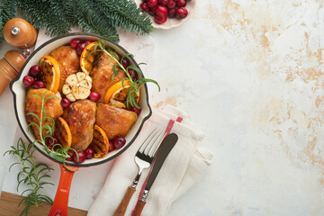 Baked chicken thighs with orange, cranberry and spicy herbs rosemary servered in frying pan on light background. Festive Christmas Dinner Concept menu. Top view. copy space