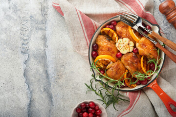 Baked chicken thighs with orange, cranberry and spicy herbs rosemary servered in frying pan on light background. Festive Christmas Dinner Concept menu. Top view. copy space