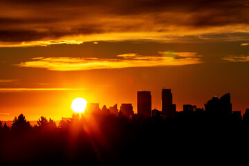 Dramatic colourful sky with a silhouetted cityscape and sunburst; Calgary, Alberta, Canada