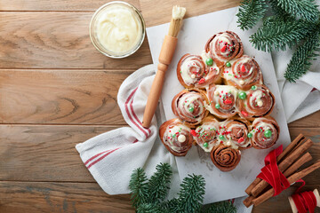 Christmas tree shape cinnamon rolls or cinnabon buns with cinnamon and cream sauce on wooden background. Festive idea for Homemade traditional winter festive dessert buns pastry for dinner. Top view.