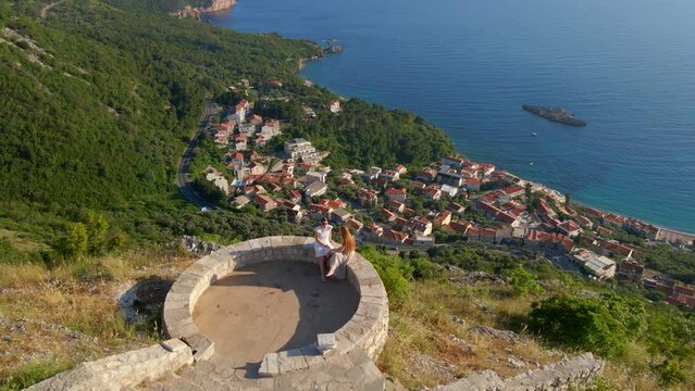 Aerial slowmotion video. Two women visit the Saint Sava church which is located above the Sveti Stefan island near the city of Budva. Travel to Montenegro concept