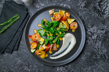 salad with shrimp, avocado, tomatoes and mango sauce on black plate