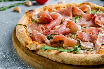 Pizza with Parma ham and arugula on wooden board on grey table macro close up