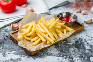 french fries on board with ketchup on grey table