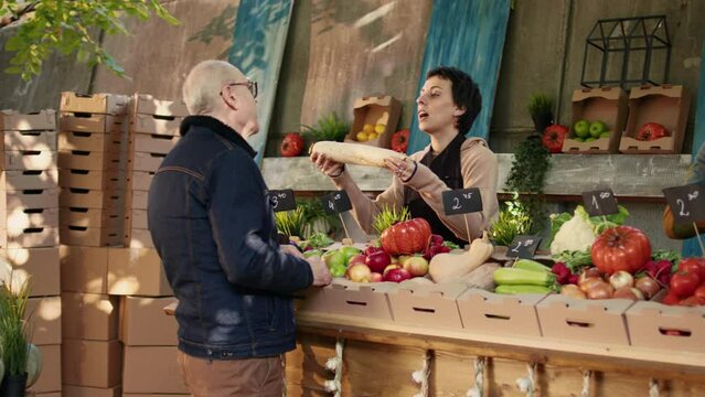 Diverse stand vendors showing colorful fruits and veggies to customers at local food farmers market. Man and woman selling eco homegrown organic produce, having bio fresh products.