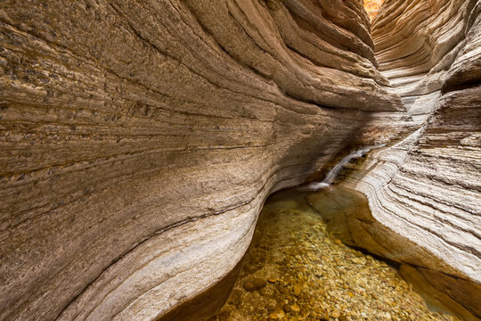 A small waterfall flows at the end of a small desert canyon.