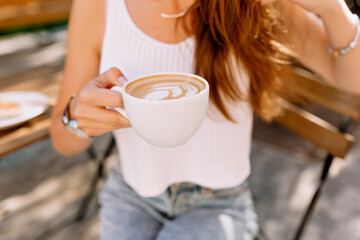 Photo from above of female hands holding white cup with coffee with milk and hot chocolate. Snapshot of glass of latte with on background of city cafe