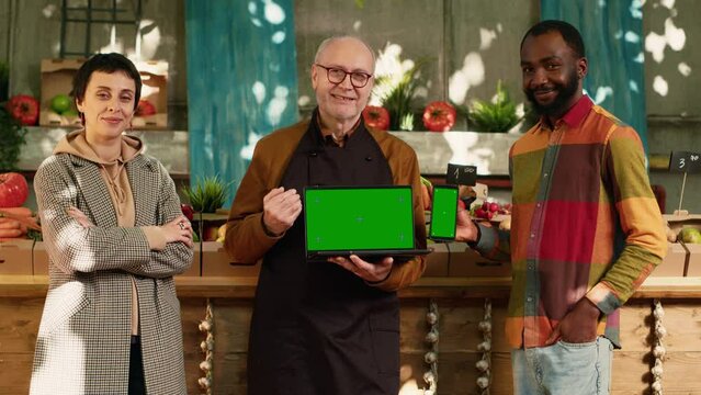 Diverse group of people showing greenscreen on laptop and smartphone, holding devices with isolated chrom key display. Farmer and clients using blank mockup template and copyspace screen.