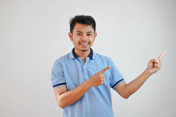 smiling asian man with fingers pointing to the side wearing blue t shirt isolated on white background