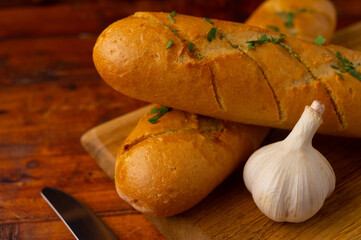 Close-up of fresh cheese garlic bread with aromatic herbs on a wooden board on a wooden table.