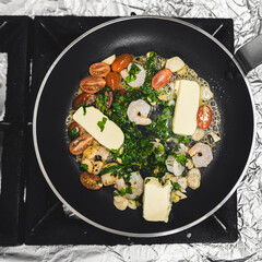 Shrimps, cherry tomatoes, parsley, and butter on frying pan. Cooking process and dish preparation. High angle view. High quality photo