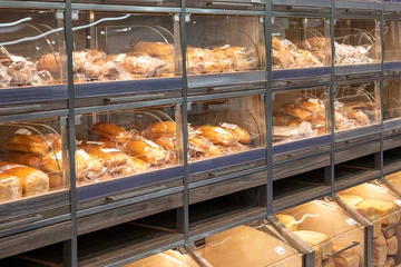 Foto op Plexiglas Fresh bread counter. Delicious loaves of bread in a baker shop. Different types of bread loaves on wooden bakery shelves. © Irina Mikhailichenko