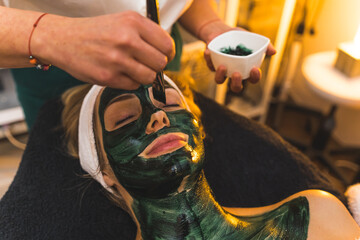 Close up of a face of a woman with black mud skin mask at a spa beauty salon. High quality photo