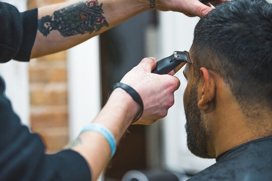 Professional barber with tattoos gromming his client's hair with electric trimmer in a barbershop. . High quality photo