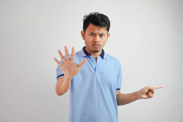 Attractive Asian man with hand gesture pose rejection or prohibition while pointing to copy space by his side wearing blue t shirt isolated on white background