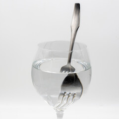 Vista de un tenedor distorsionado  dentro de una vaso lleno de agua, demostrando la refracción de...