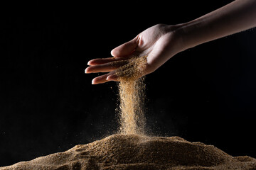 Fototapeta na wymiar Hand releasing dropping sand. Fine Sand flowing pouring through fingers against black background. Summer beach holiday vacation and time passing concept. Isolated high speed shutter