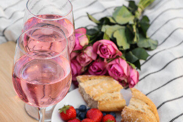 Glasses of delicious rose wine, flowers and food on white picnic blanket, closeup