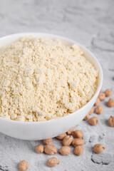 Chickpea flour in bowl and seeds on light grey textured table, closeup
