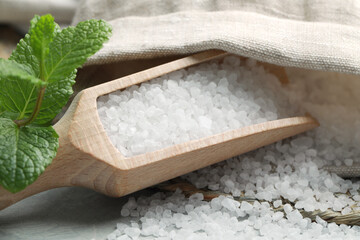 Wooden scoop with natural sea salt, sack and mint on light grey marble table, closeup