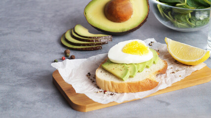 Delicious sandwich with boiled egg, pieces of avocado and lemon wedge on gray table