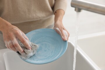 Woman washing plate above sink in modern kitchen, closeup