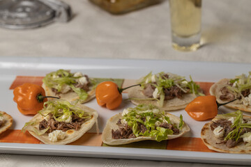 Close up of Chalupas, Typical Mexican dish made with tortillas, sauce, cheese, meat and lettuce on white tablecloth