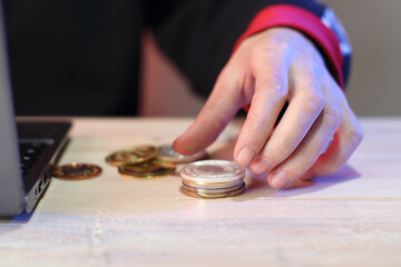 calculation of a pile of coins on a table next to a laptop by a person