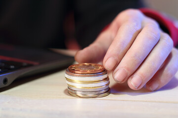 calculation of a pile of coins on a table next to a laptop by a person
