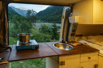 View out of a self built camper van with gas running stove outside to green mountain landscape with...