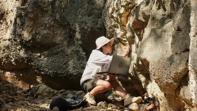 Female geologist using laptop computer examining nature, analyzing rocks or pebbles. Researchers collect samples of biological materials. Environmental and ecology research.
