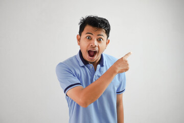 shocked asian man with an open mouth with fingers pointing to the side wearing blue t shirt isolated on white background