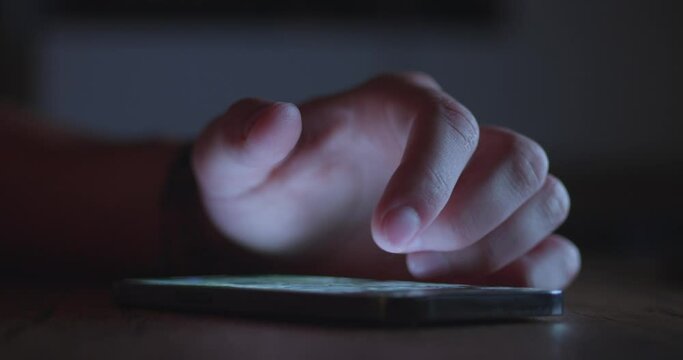 Close-up: male hand using smartphone at night at the table indoors.
