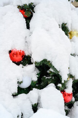 A fragment of a Christmas tree decorated with colored glass balls on the street under a snowfall