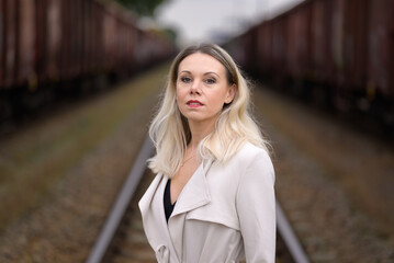 Woman in a white trench coat in front of train wagons