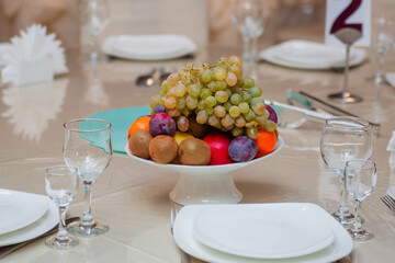 Table setting. Fresh fruits in a vase tangerines and green grapes. Kiwi and plums.