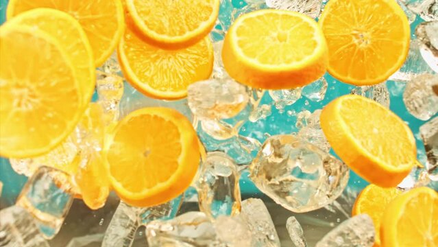 Juicy sweet orange and fly ice cube or water splash or pouring drops juice in super slow motion on 1000 fps. Citrus orange slices and ice fall or explode on blue background, super slow motion 1000fps