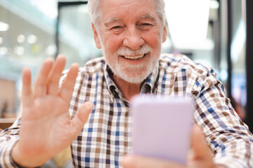 Portrait of happy caucasian senior man video talking on mobile phone in video call - handsome bearded elderly man sitting using smartphone