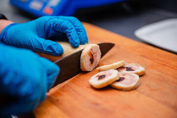 Hands in blue gloves cut meat snack roll with dried apricots and prunes.