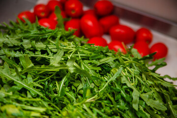 Arugula with tomatoes for salad preparation.