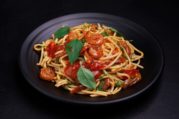 Delicious spaghetti pasta with prawns and cheese served on a black plate. With vegetables, Italian tomato sauce, and spices arranged on a wooden table, black background, top view