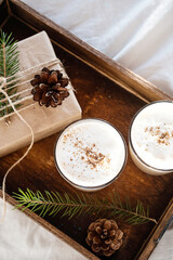 Christmas cozy morning in bed. Gift box and eggnog on wooden tray on white bedding.