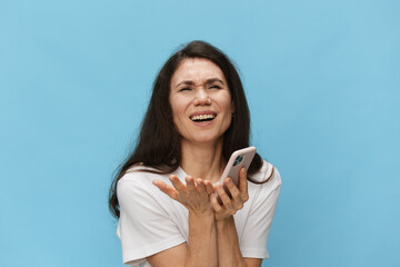Fototapeta premium A sad, depressed, emotional woman holds out her fashionable phone to the camera, expressing terrible sadness on her face. Horizontal photo with space for an advertising insert