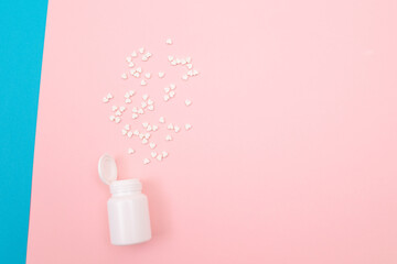 Global Pharmaceutical Industry and Medicinal Products - White Pills or Tablets Scattered from the Pill Container, Lying on Split Blue and Pink Background