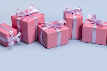 Gifts in pink boxes, decorated with satin ribbon. Concept for greeting card, frame, banner. Blue background, studio shot.