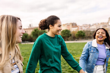 Muslim young woman having fun with diverse female friends outdoors. International friendship concept with three multi-ethnic millennial females holding hands showing unity and community