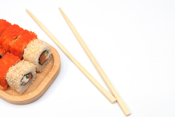 Delicious Japanese rolls with salmon, avocado, cucumber, cheese on wooden plate with wood sticks with selective focus on white background. Asian food concept. Healthy eating